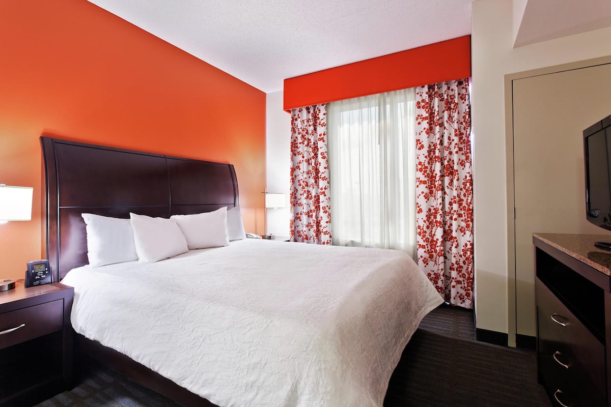 Quarto de hotel com uma cama grande, mesa de cabeceira com telefone e televisão em uma cômoda.