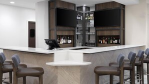 A modern bar area with a white countertop, bar stools, and shelves stocked with bottles and glasses. - Hilton Garden Inn Indianapolis Northeast/Fishers (Fishers)