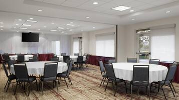 A conference room with round tables and chairs, a flat-screen TV, and large windows with blinds.