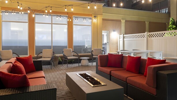 A well-lit outdoor seating area with wicker furniture and red cushions, overlooking a cityscape. - Hilton Garden Inn Indianapolis Northeast/Fishers (Fishers)
