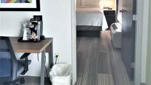 A hotel room with a bed, bedside table, and a desk with a coffee machine. There is a trash bin and a framed picture on the wall. - Holiday Inn Express & Suites San Antonio-West-SeaWorld Area by IHG (San Antonio)