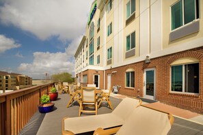 Ein Hotel mit Außenbereich und überdachter Terrasse, inklusive Liegestühlen und Tischen, sowie ein Ziegelgebäude mit zahlreichen Fenstern.