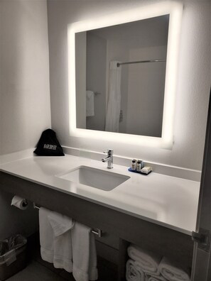 Un baño con un espejo grande, un lavamanos y un perchero para toallas.