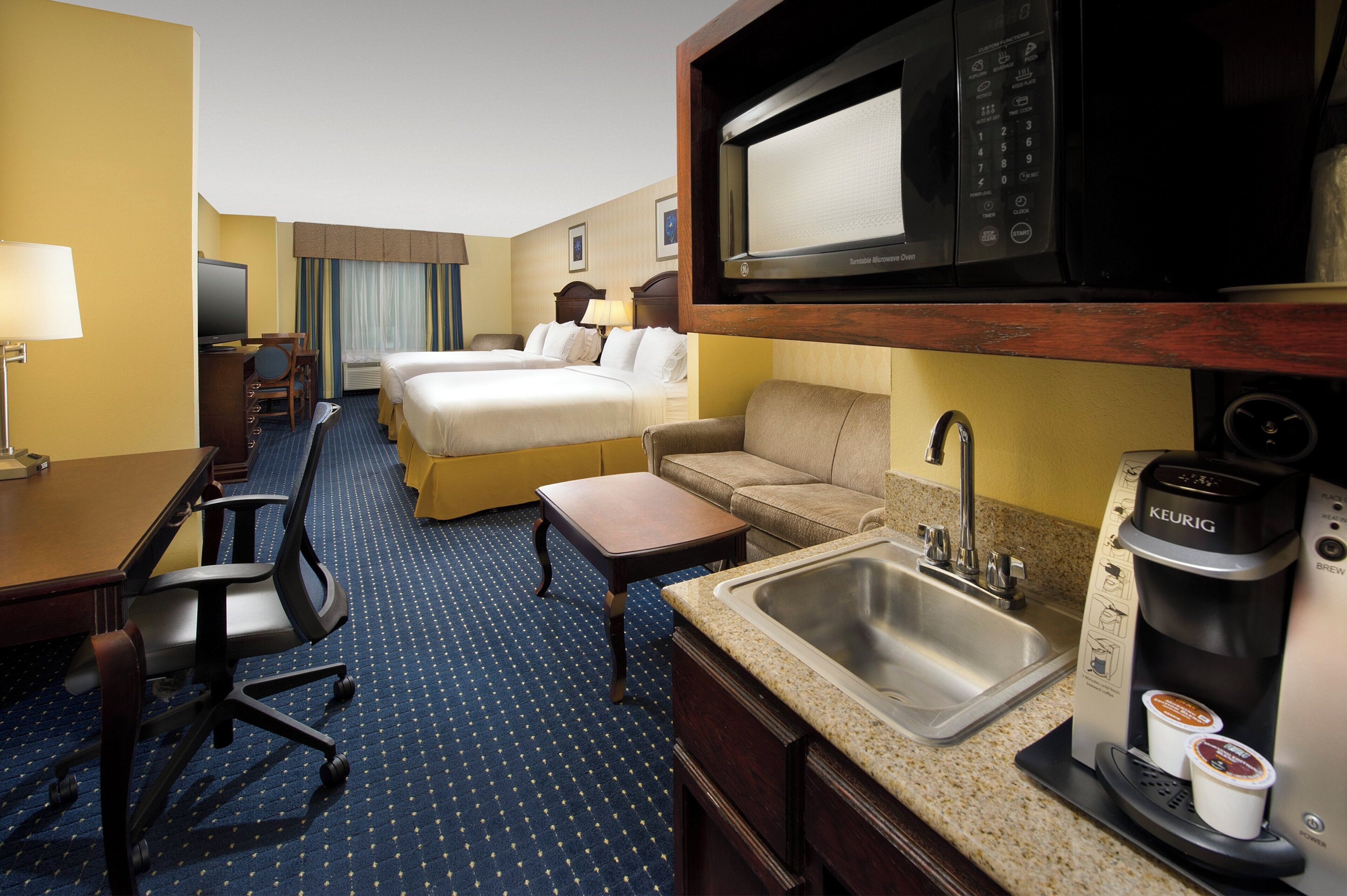 Een hotelkamer met een bed, bureau, stoel, bank, magnetron, koffiezetapparaat en wastafel.