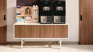 Una estación de café con dos máquinas de café, un estante con tazas y un área de almacenamiento con cajas y una tetera.