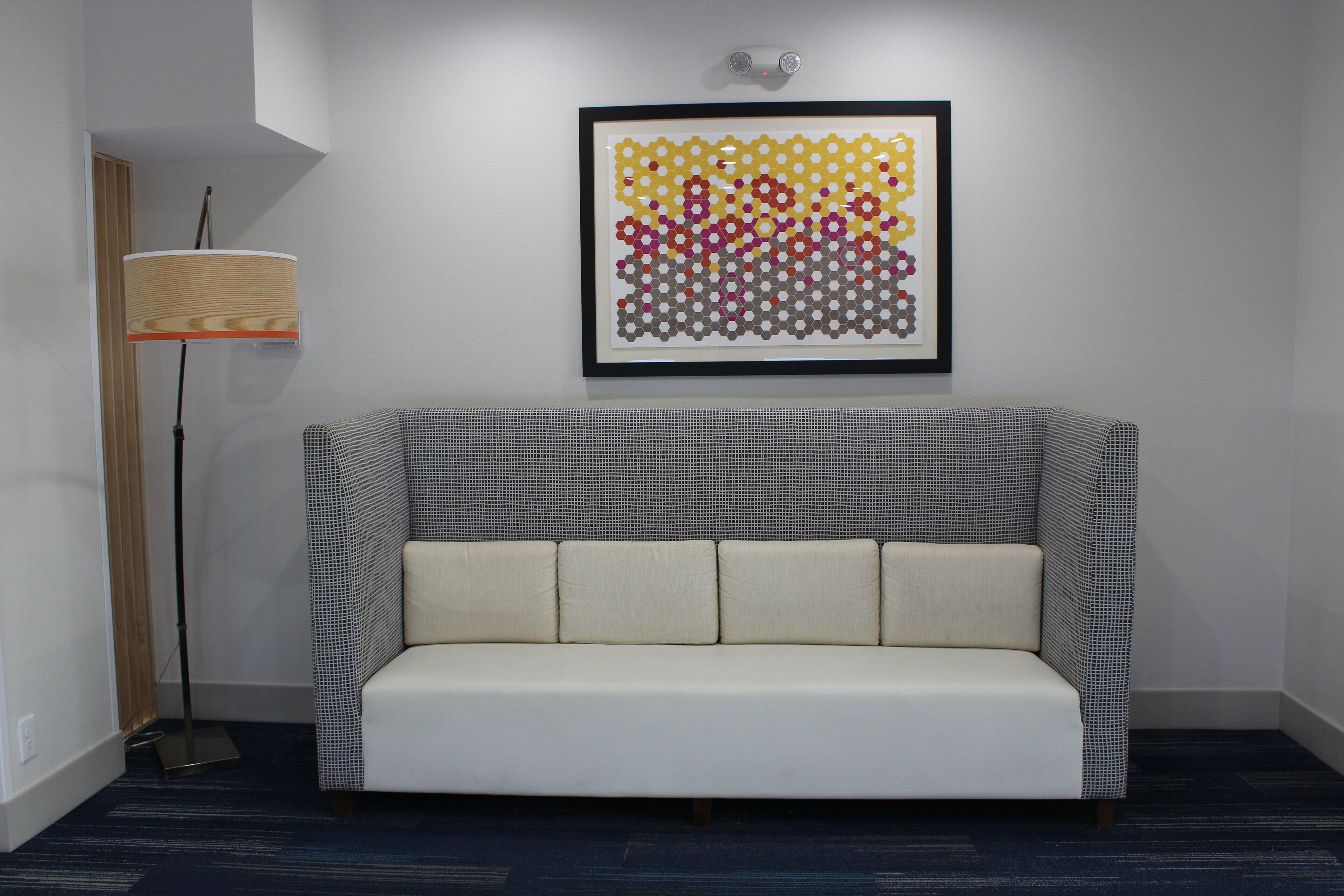 A modern living room with a patterned sofa, a floor lamp, and a framed abstract art piece on the wall.