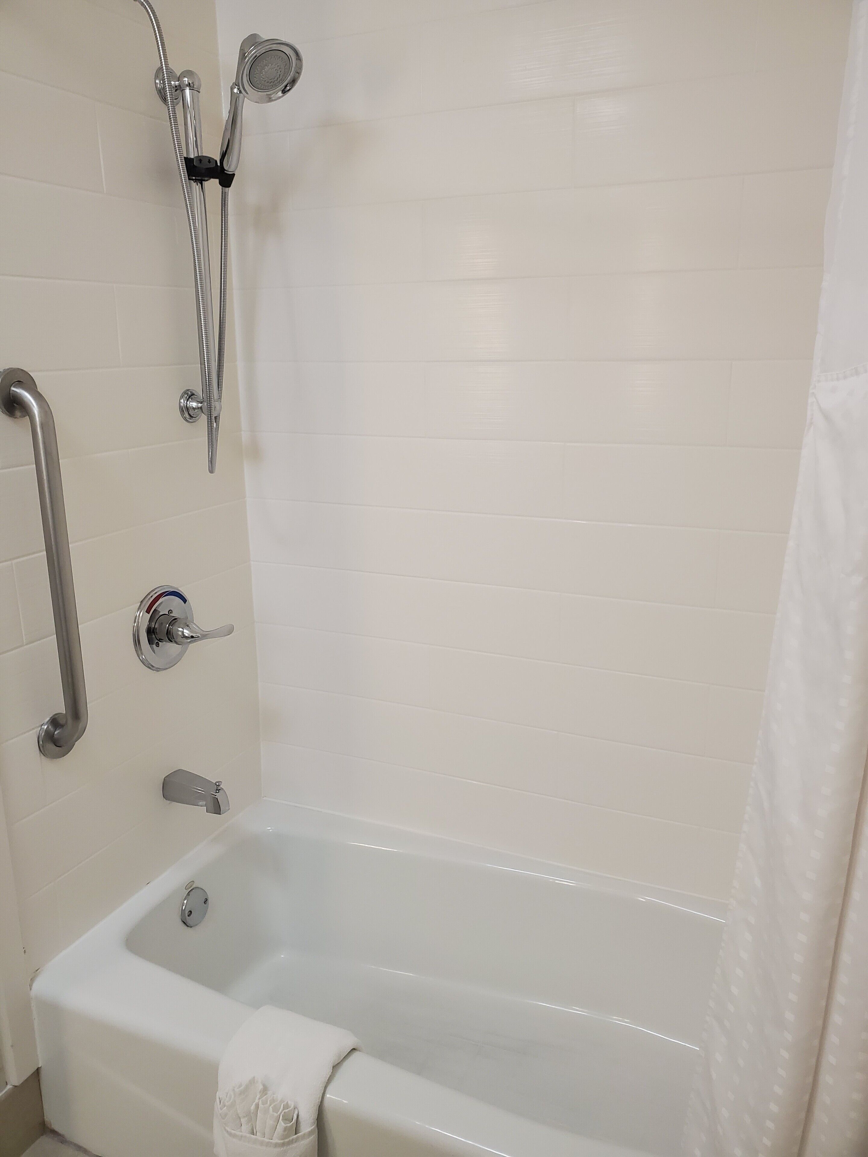 A bathroom with a bathtub, a shower with a handheld showerhead, and a grab bar.