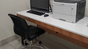Un espacio de trabajo con una computadora portátil, una impresora y una silla de oficina negra.