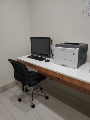 Un espacio de trabajo con una computadora portátil, una impresora y una silla de oficina negra.