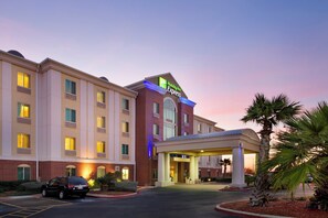 Um hotel Holiday Inn Express com entrada coberta, estacionamento e uma palmeira em primeiro plano.