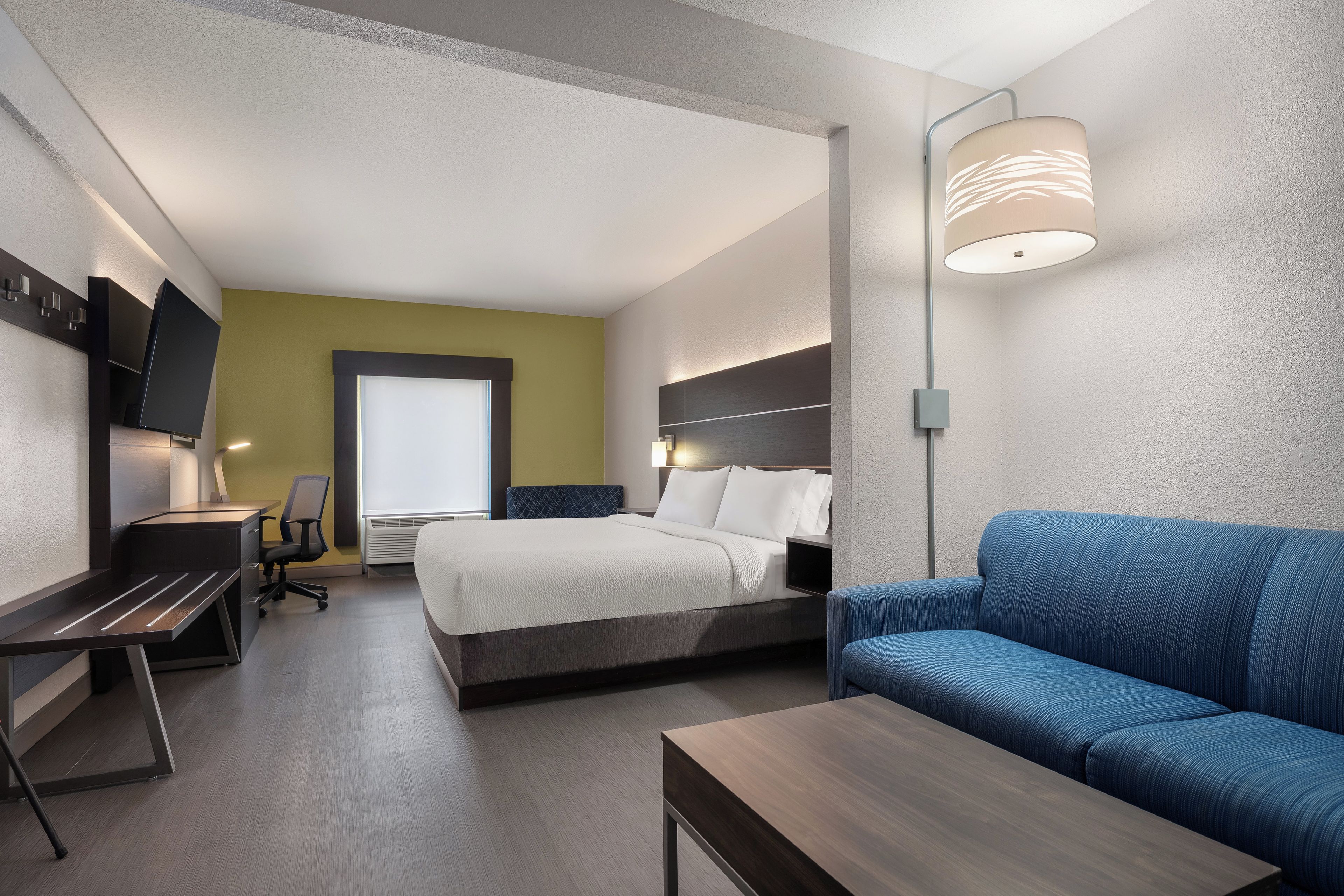 A hotel room with a bed, a desk, a chair, a sofa, and a TV.