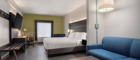 A hotel room with a bed, a desk, a chair, a sofa, and a TV.
