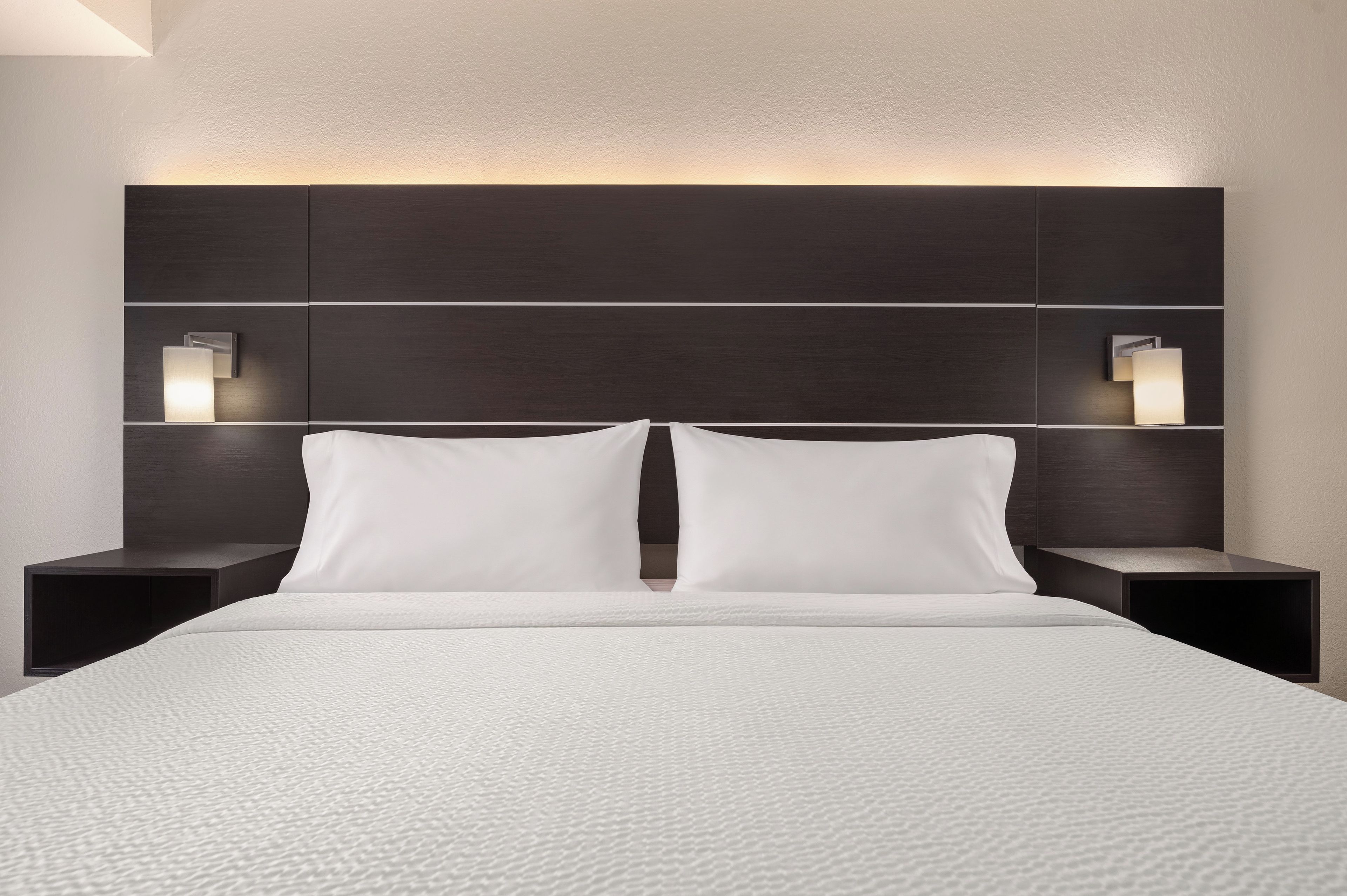 Una habitación de hotel moderna con una cama grande, dos mesitas de noche y lámparas de pared.