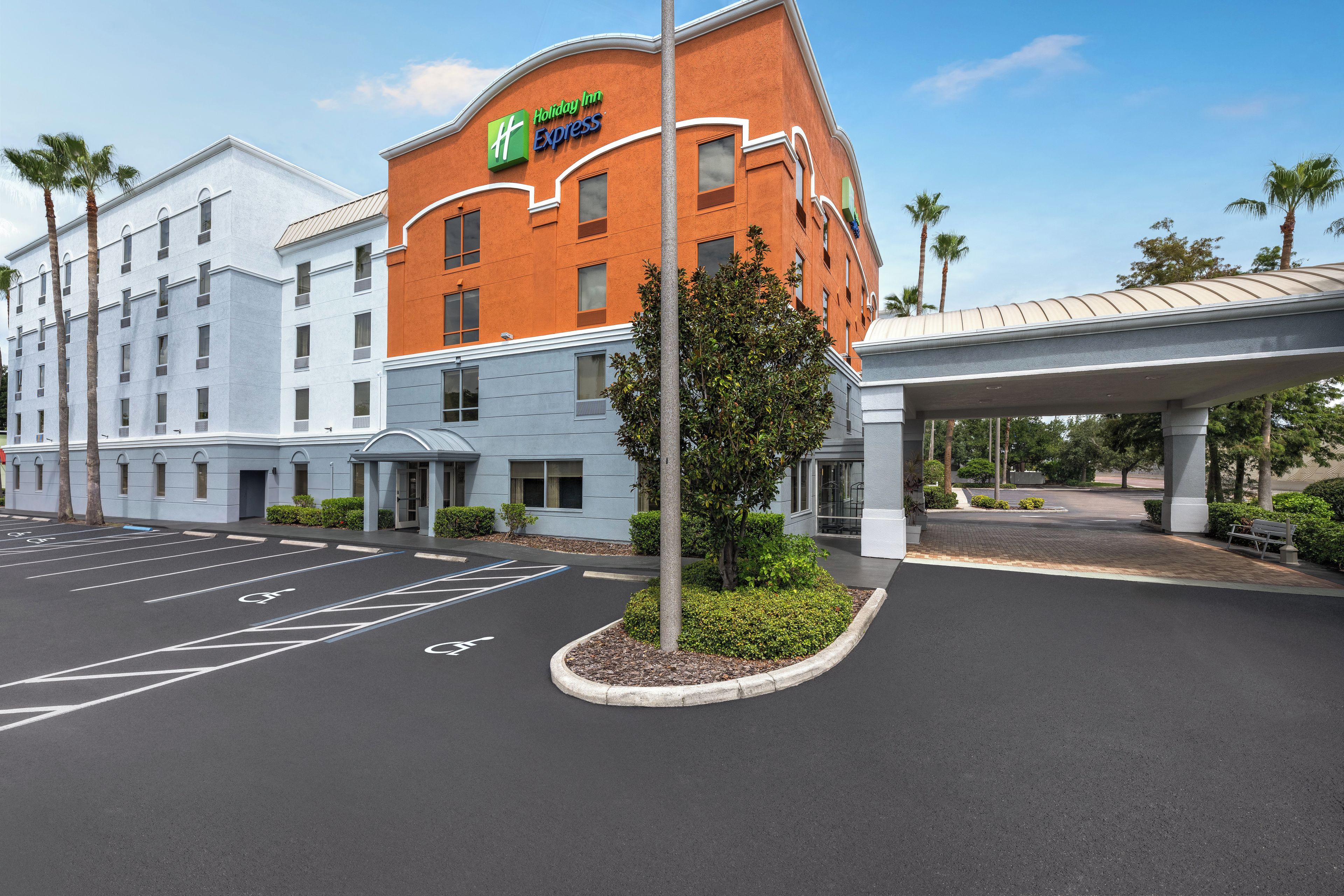 A Holiday Inn Express hotel with a parking lot, a covered walkway, and a landscaped area with a palm tree.