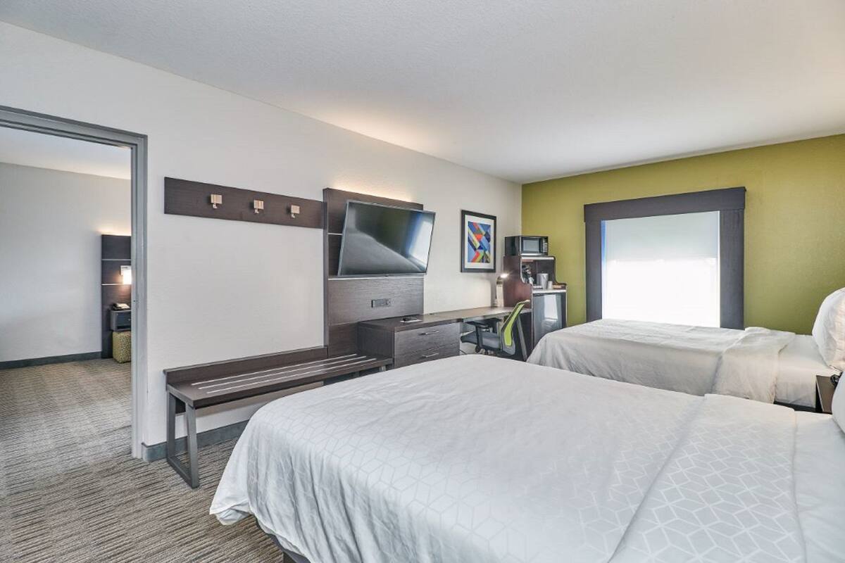 A hotel room with two beds, a desk with a computer, a TV, and a coffee machine.
