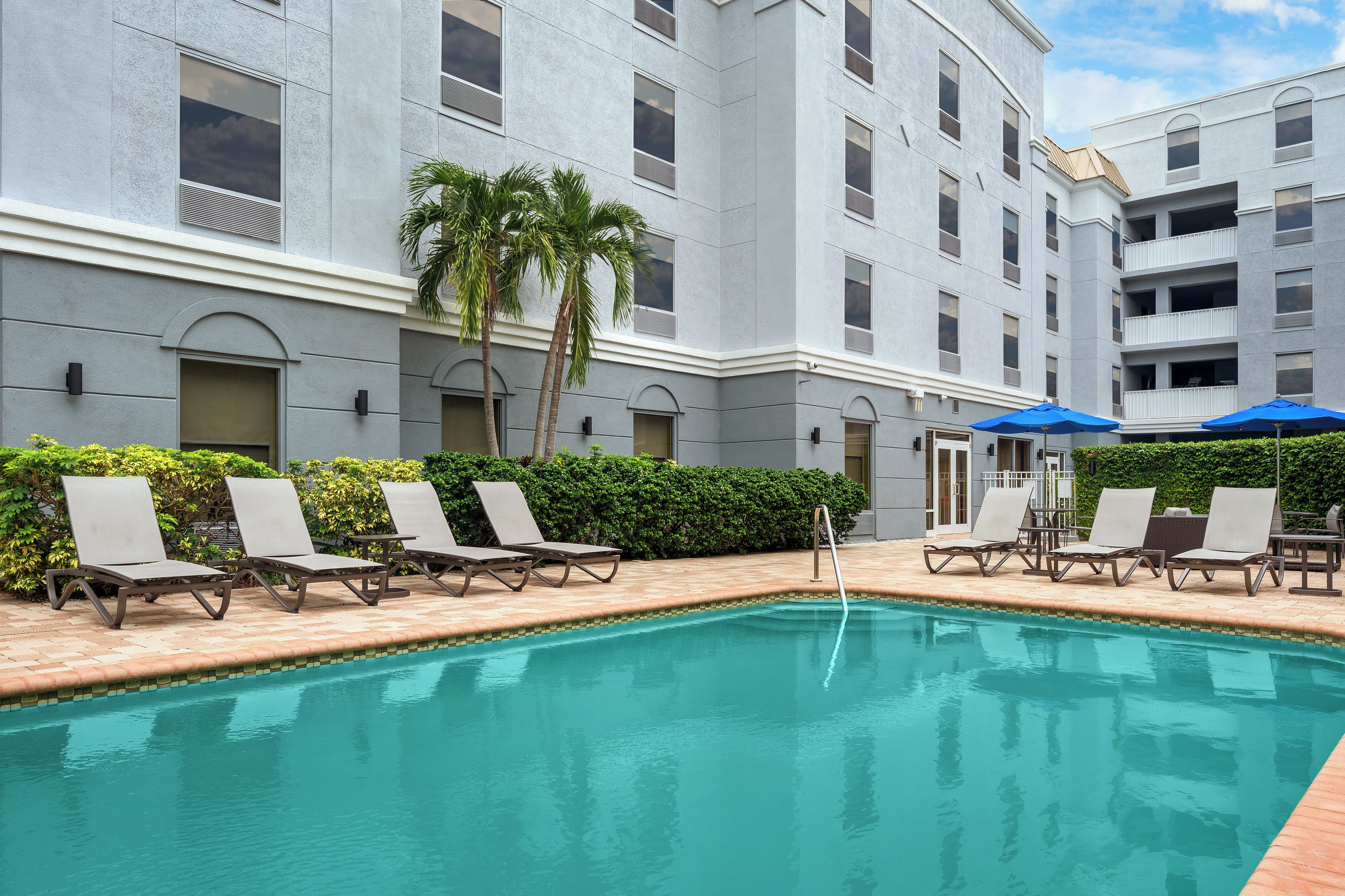 A swimming pool with lounge chairs and umbrellas, surrounded by a building with multiple balconies and windows.
