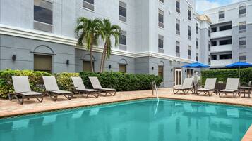 A swimming pool with lounge chairs and umbrellas, surrounded by a building with multiple balconies and windows.
