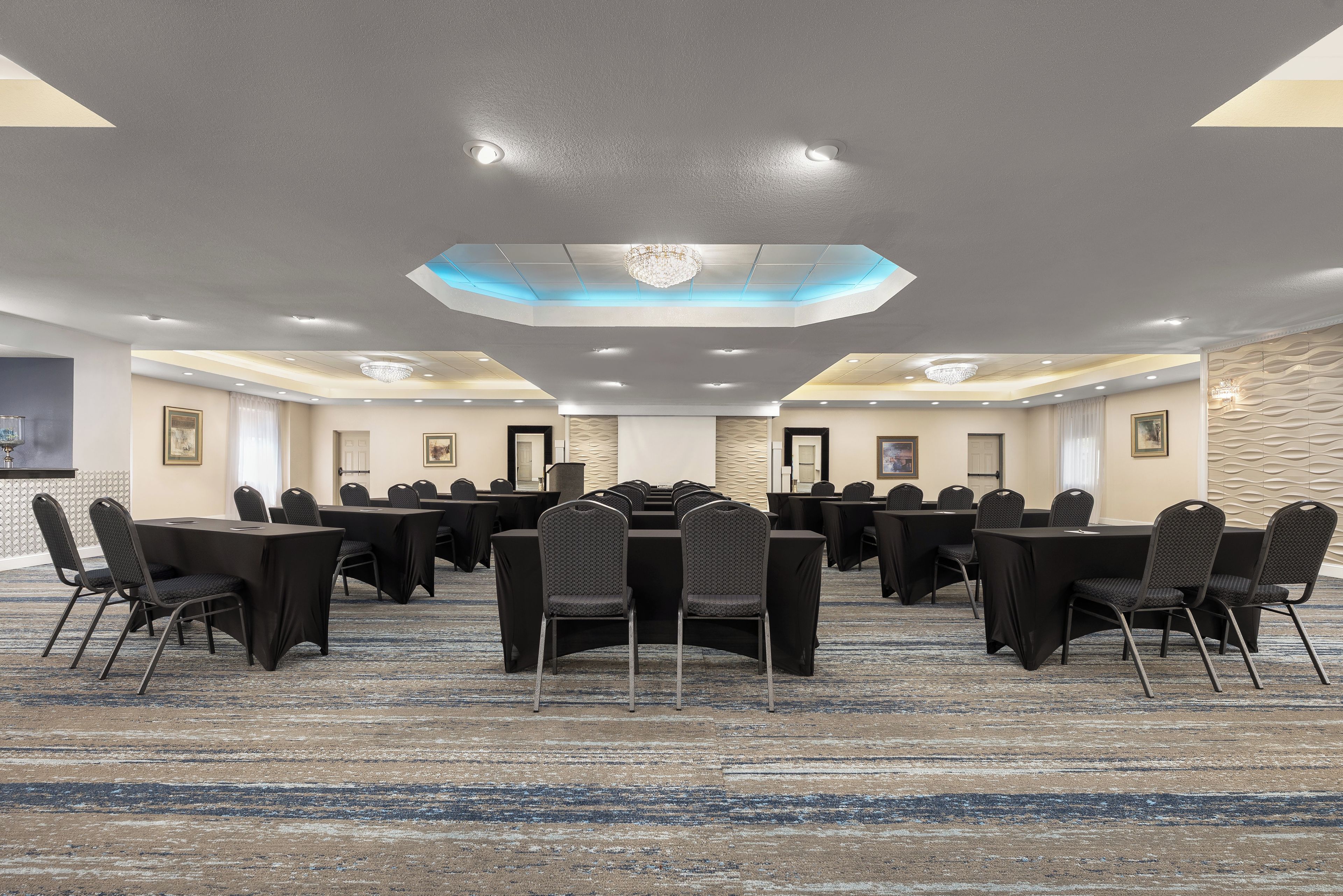 Un salón de conferencias con varias mesas y sillas, una alfombra estampada y un diseño de techo moderno.