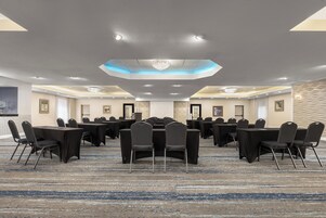 Un salón de conferencias con varias mesas y sillas, una alfombra estampada y un diseño de techo moderno.