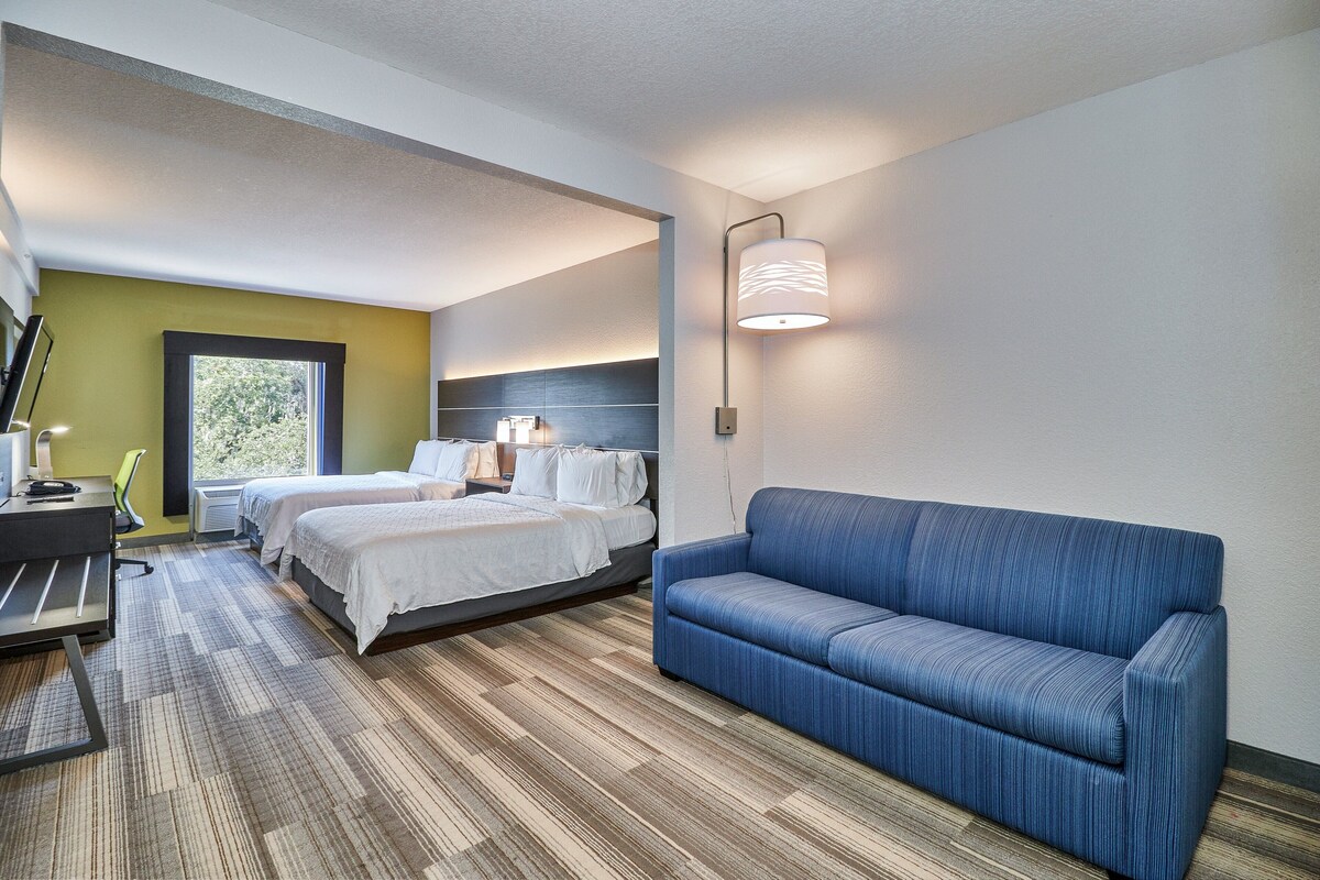 Habitació d'hotel amb un llit, dues taules de nit, un escriptori amb una cadira, un sofà blau i una làmpada penjada a la paret.