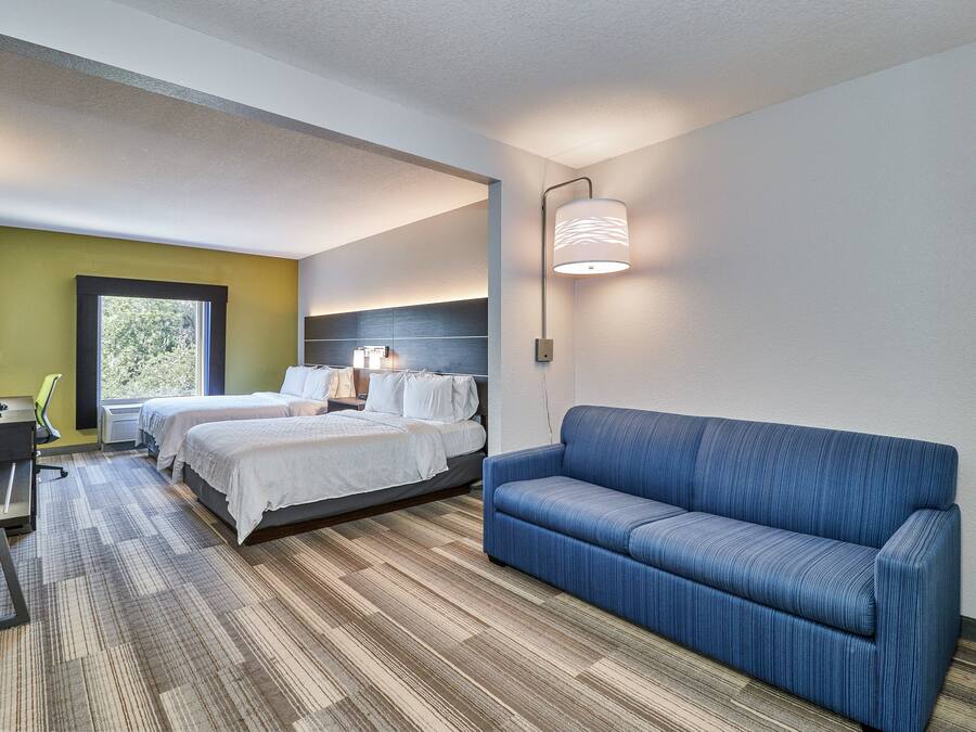 A hotel room with a bed, a desk, a chair, a sofa, and a window.
