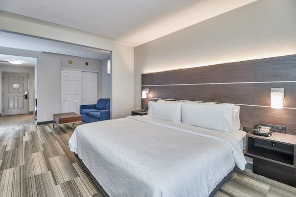 Una habitación de hotel con una cama grande, un escritorio con teléfono, una silla y una lámpara en la pared.