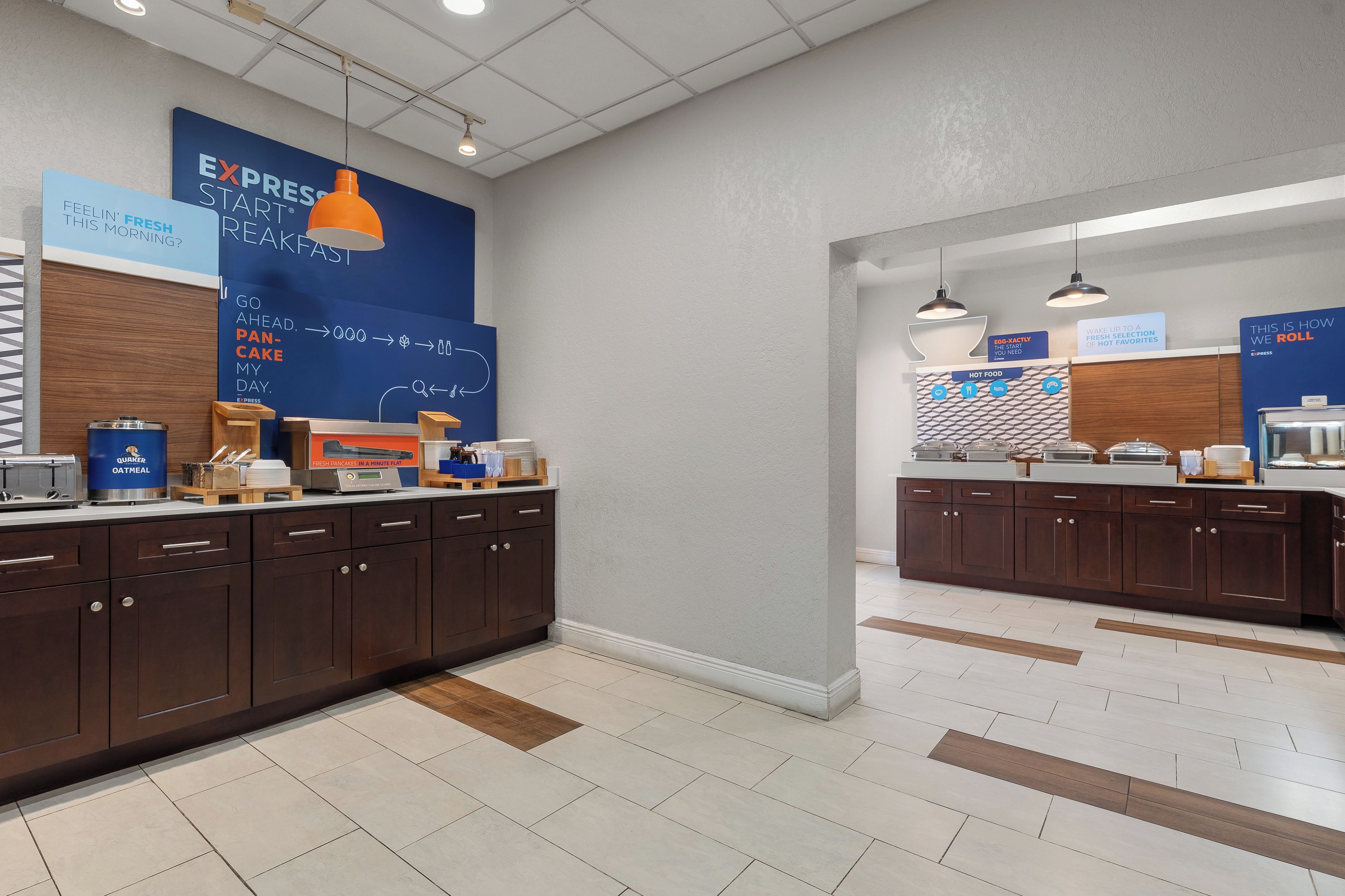 A modern kitchen area with a breakfast bar, a blue wall with breakfast-related text, and a sign indicating hot food options.