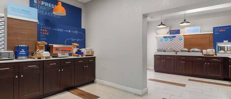 A modern kitchen area with a breakfast bar, a blue wall with breakfast-related text, and a sign indicating hot food options.
