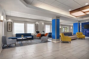 Un hall d’entrée spacieux avec un canapé bleu, une table basse et un coin salon doté de fauteuils jaunes et gris.