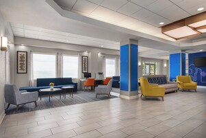 A spacious lobby with a blue sofa, a coffee table, and a seating area with yellow and grey chairs.