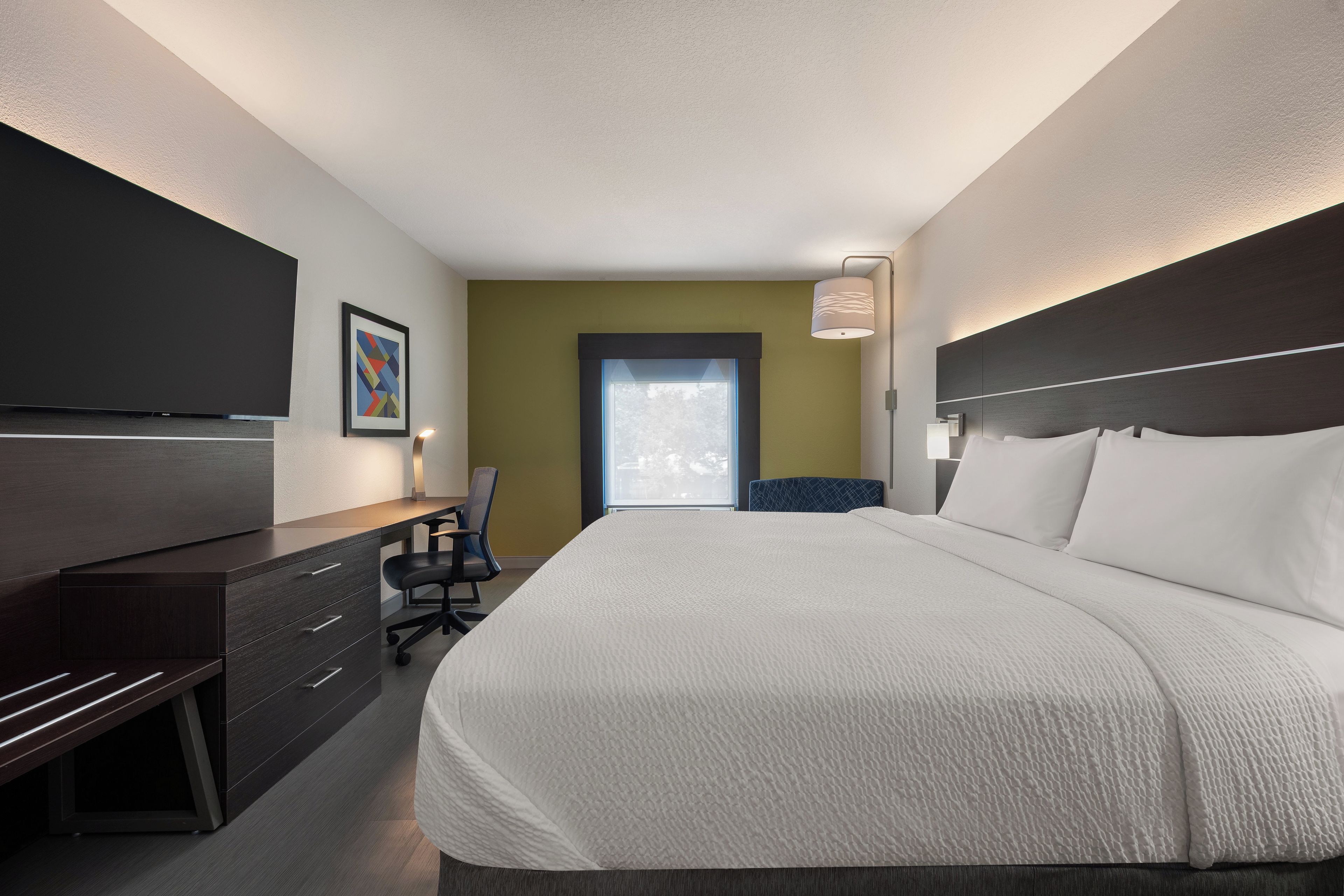 Ein Hotelzimmer mit Bett, Schreibtisch, Stuhl, Fernseher und einem Fenster.