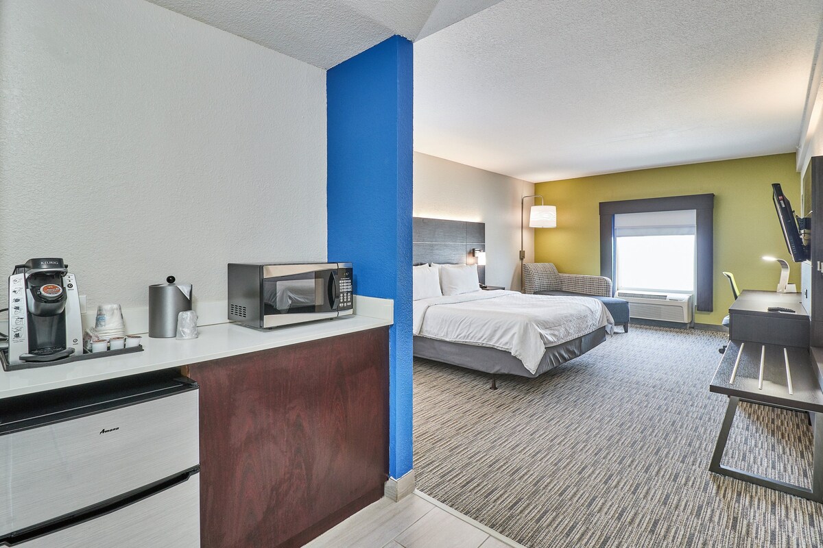 Habitació d'hotel amb cuina americana, un llit, una taula de treball i una finestra amb vistes.