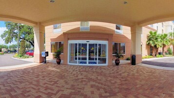 A hotel entrance with a covered walkway, a revolving door, and potted plants.