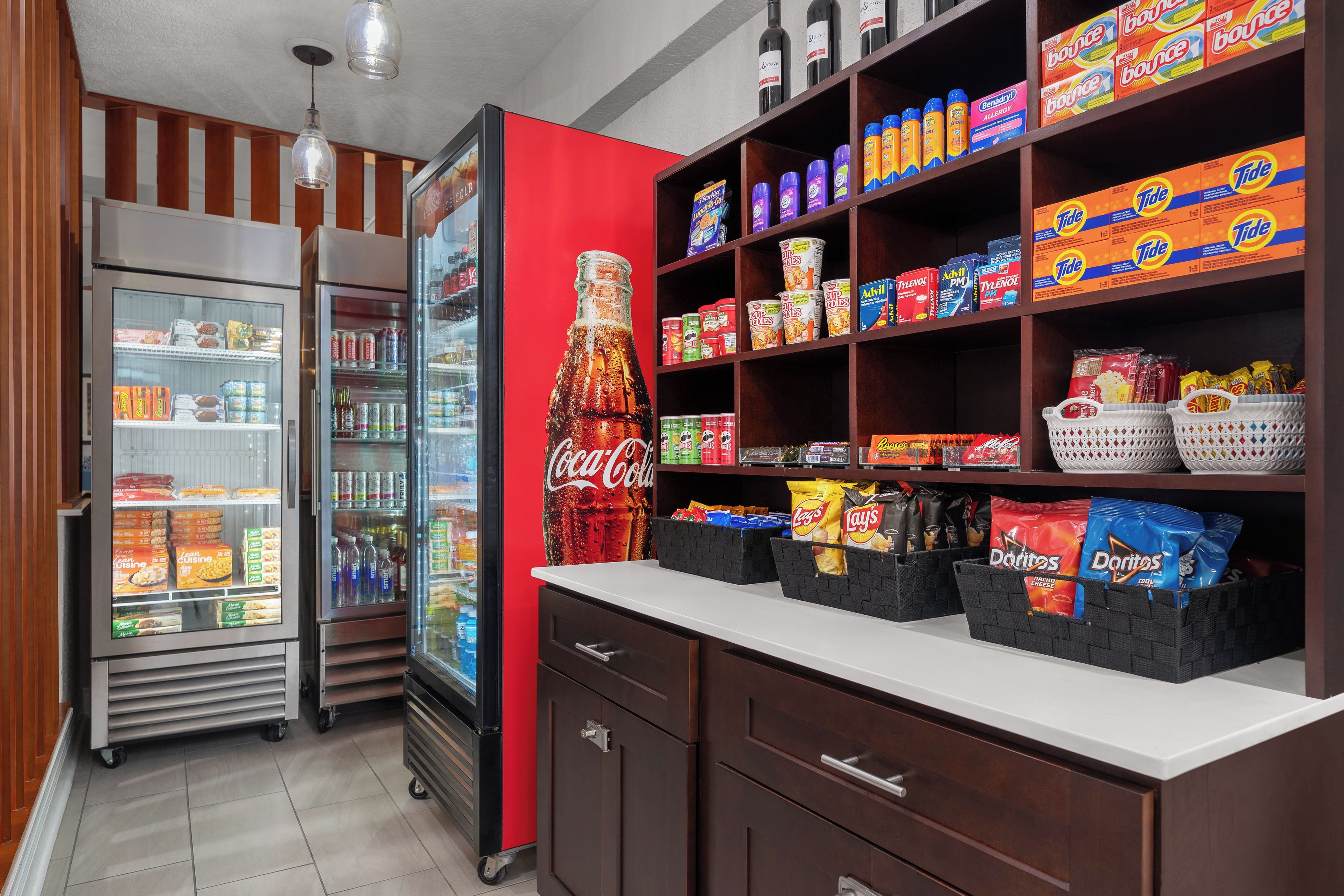 A kitchenette with a refrigerator, a microwave, a soda cooler, and shelves stocked with snacks and beverages.