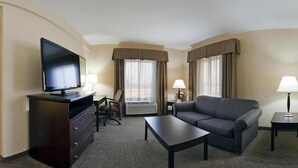 Una habitación de hotel con un televisor de pantalla plana sobre una cómoda, un sofá, una mesa de centro y dos lámparas.