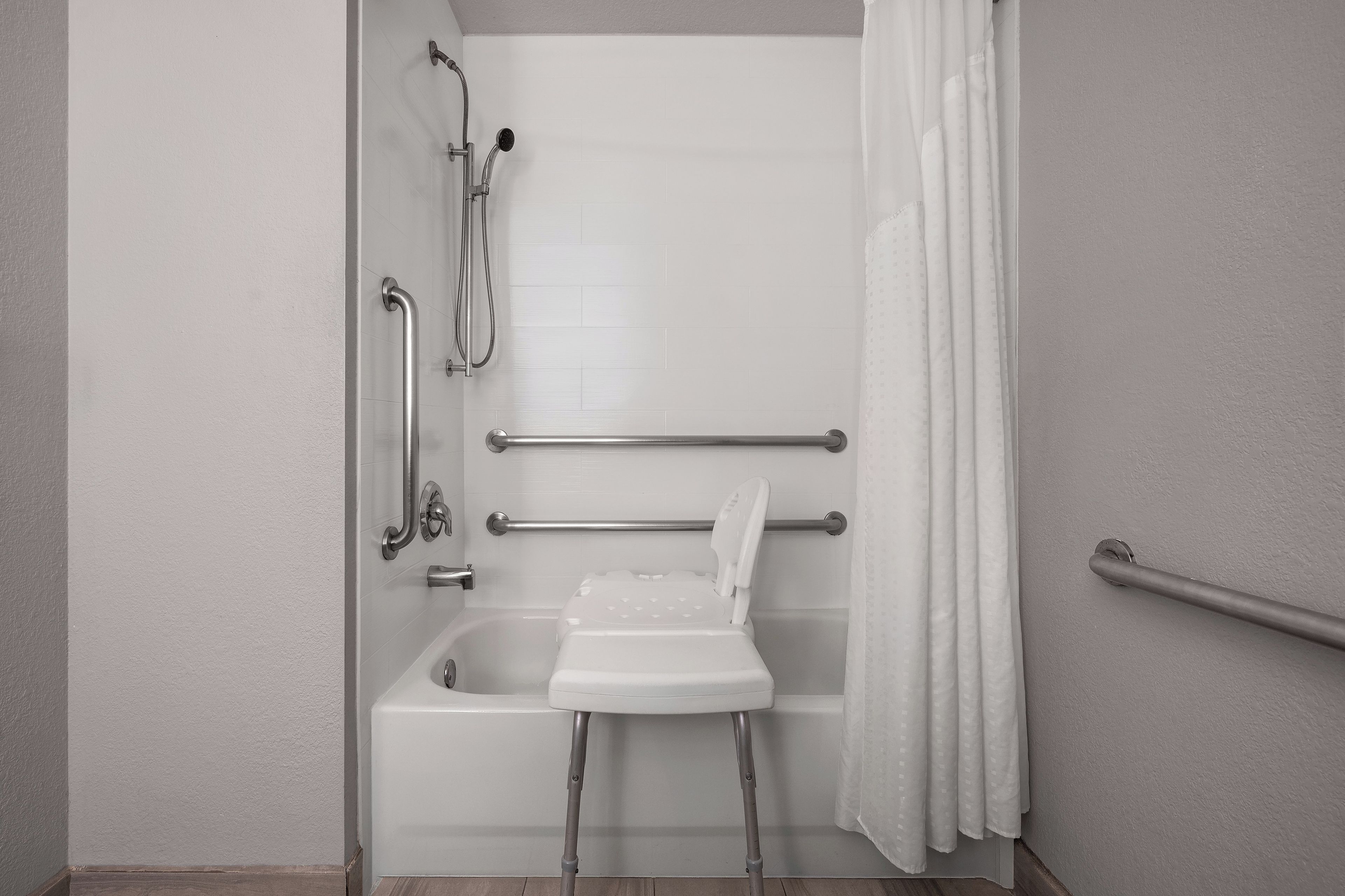 A bathroom with a shower, grab bars, and a wheelchair-accessible bench.