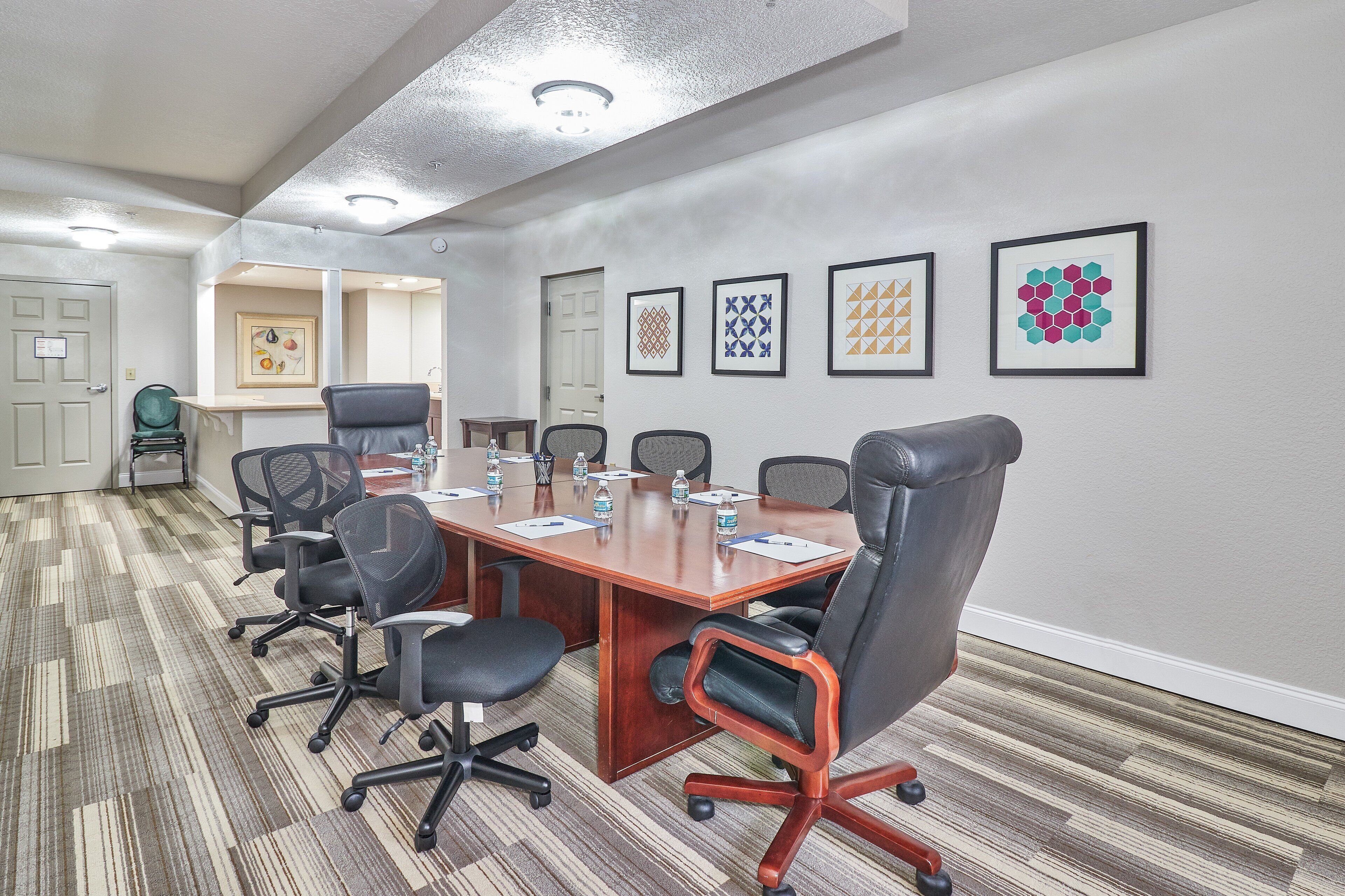 A conference room with a long table, six chairs, and framed artwork on the wall.