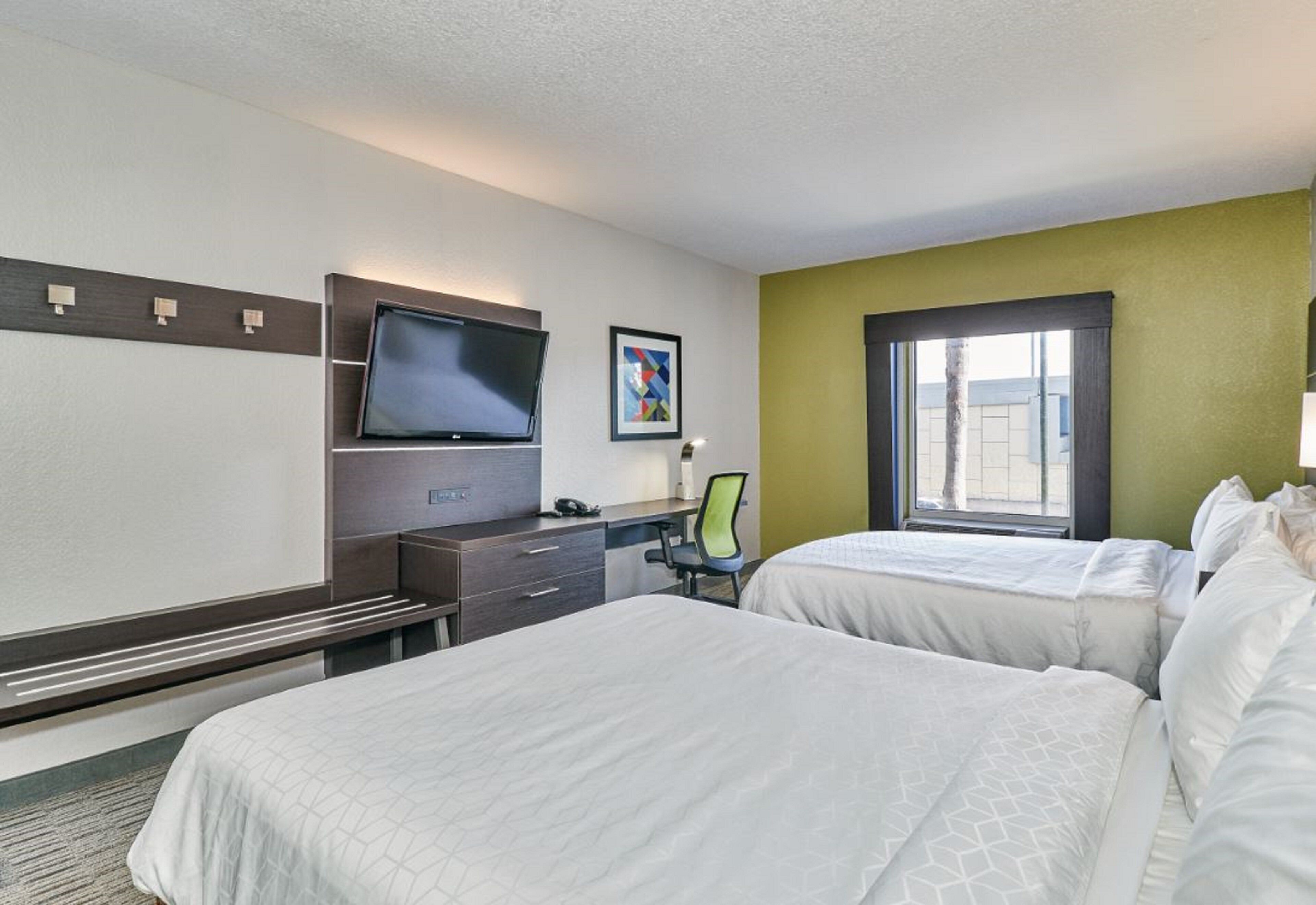 A hotel room with two beds, a desk, a flat-screen TV, and a window.