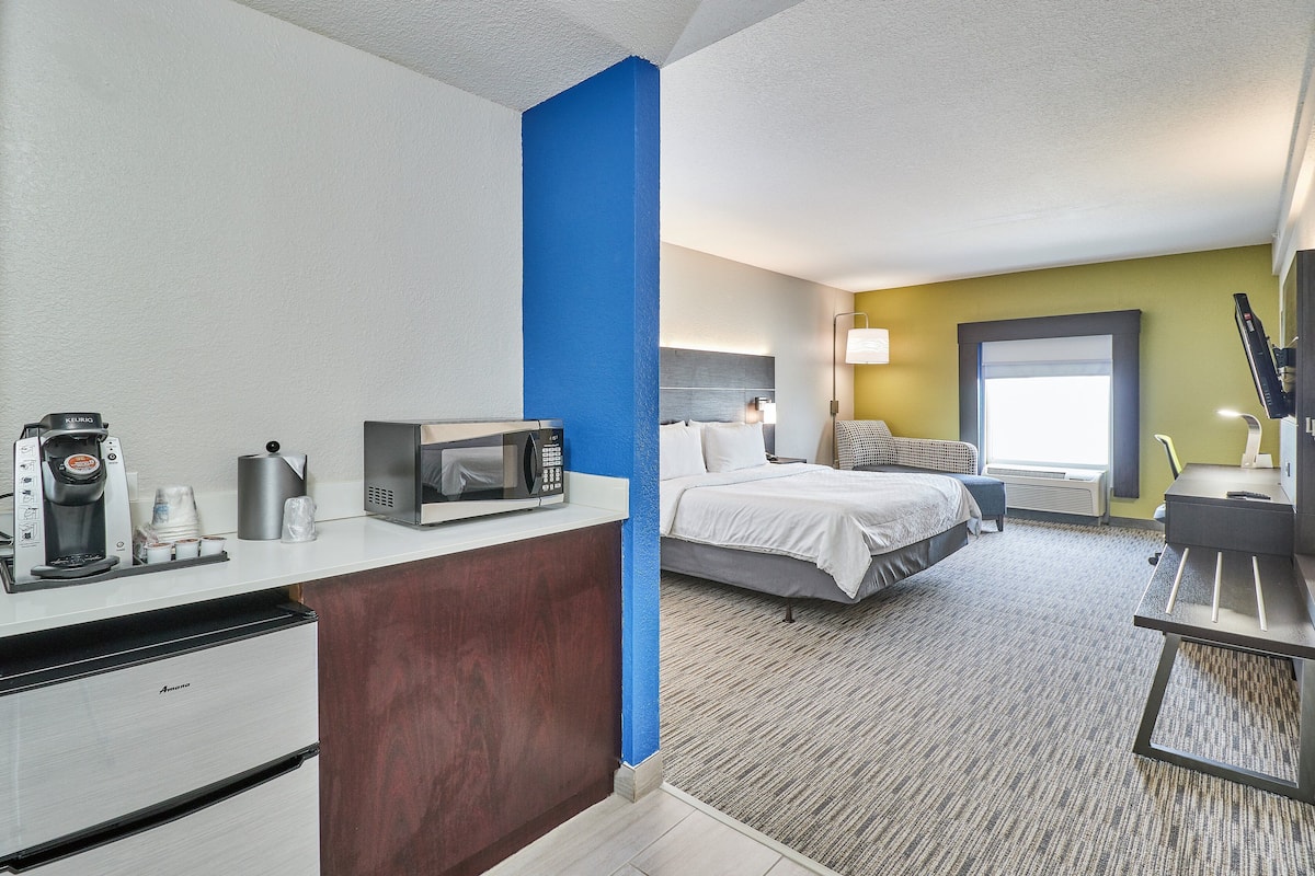 A hotel room with a kitchenette, a bed, a desk, and a window with a view.