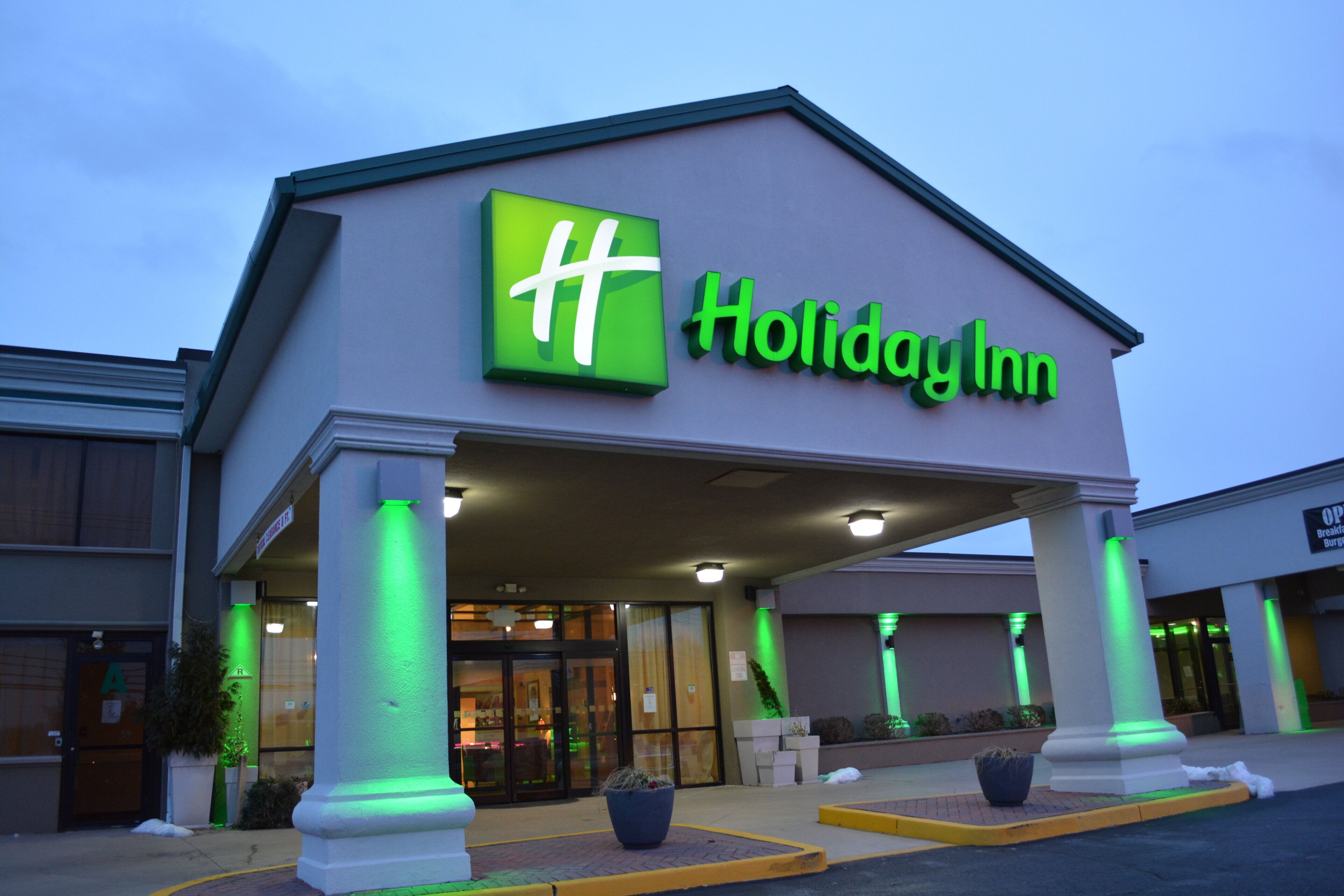 A Holiday Inn hotel entrance with a prominent sign, columns, and potted plants.