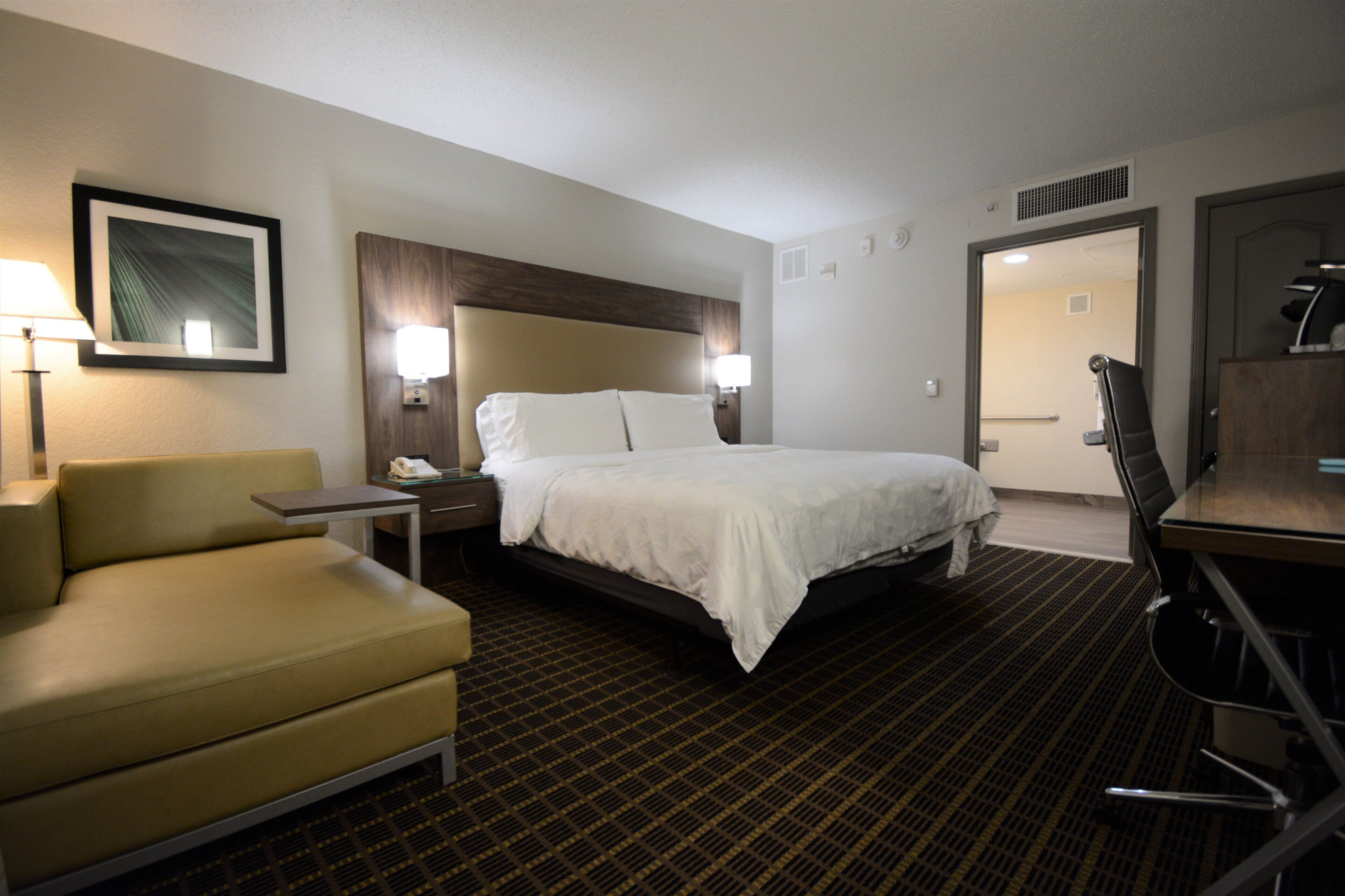 A hotel room with a bed, a chair, a desk, and a lamp.