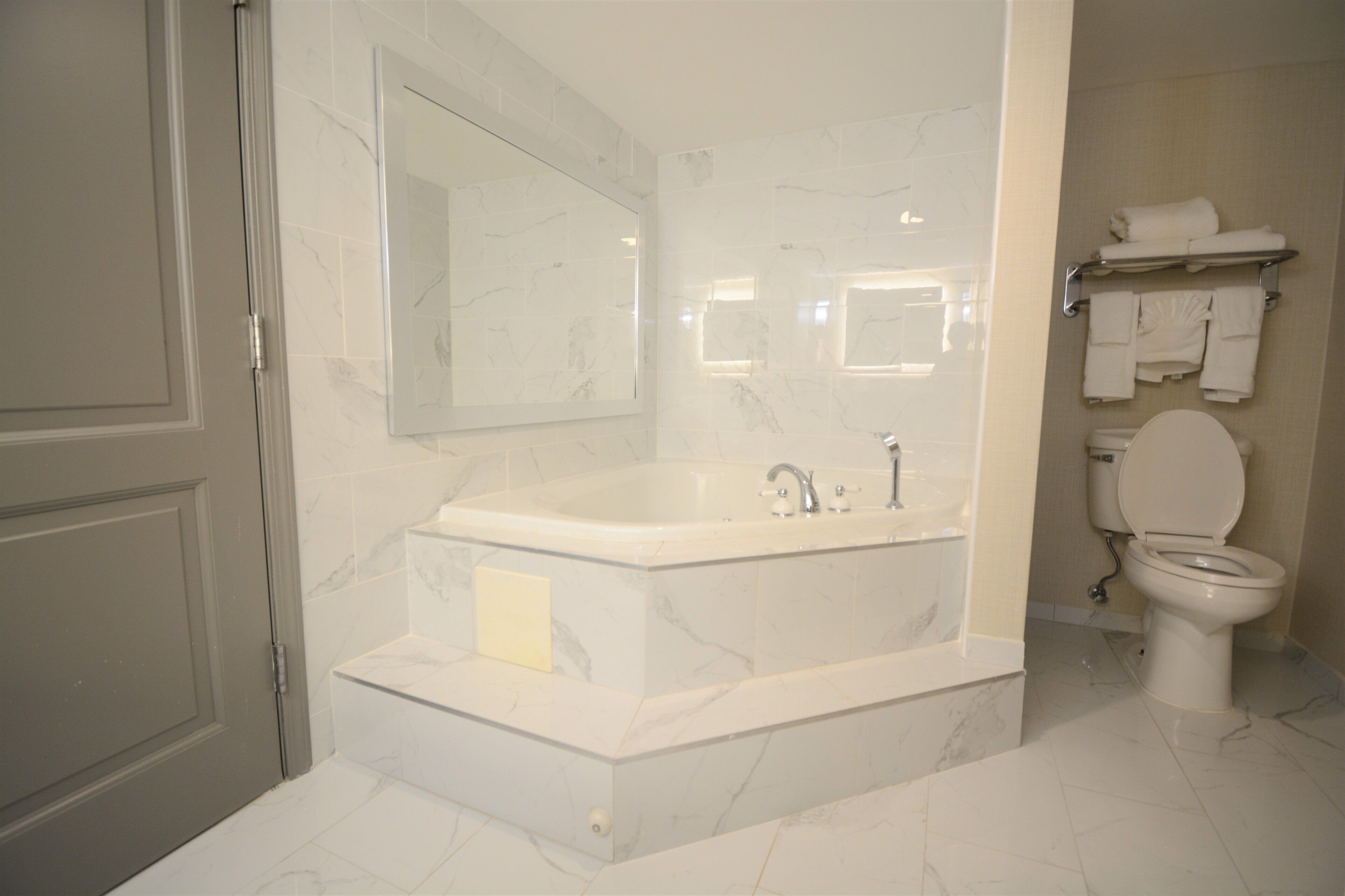 Un baño con una bañera grande, un inodoro y un espejo.