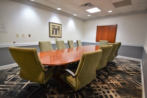 Un salón de conferencias con una mesa rectangular rodeada por seis sillas, un cuadro enmarcado en la pared y un panel de madera.