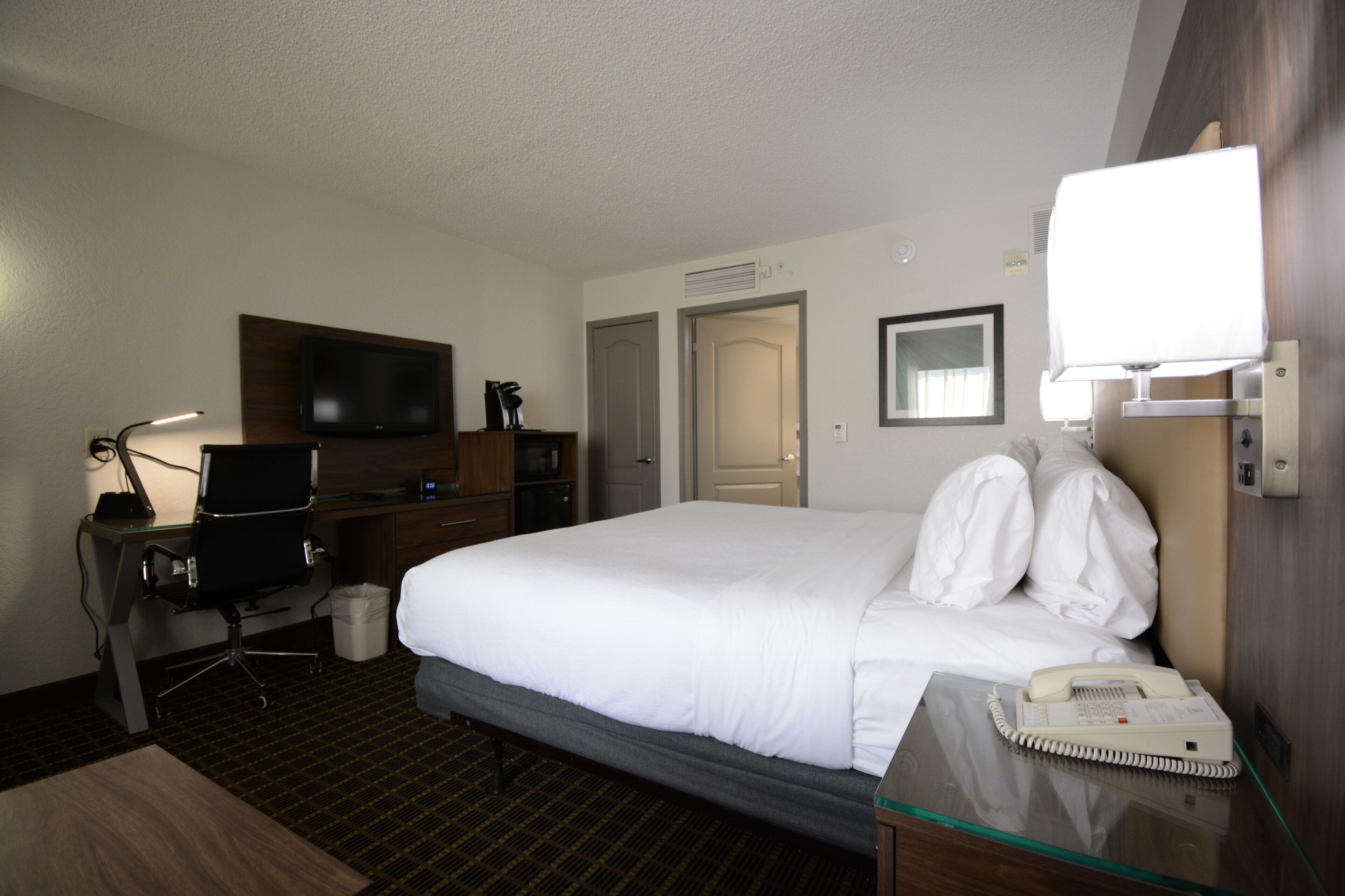 A hotel room with a bed, a desk with a computer, a television, and a telephone.
