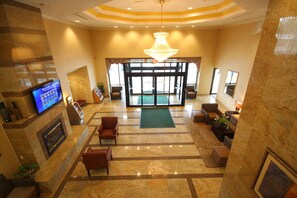A lobby with a chandelier, seating area, and a television displaying weather information. - Holiday Inn Hazlet by IHG (Hazlet)