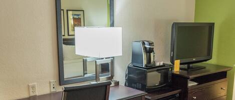 A hotel room with a desk, chair, television, coffee maker, and a trash bin.