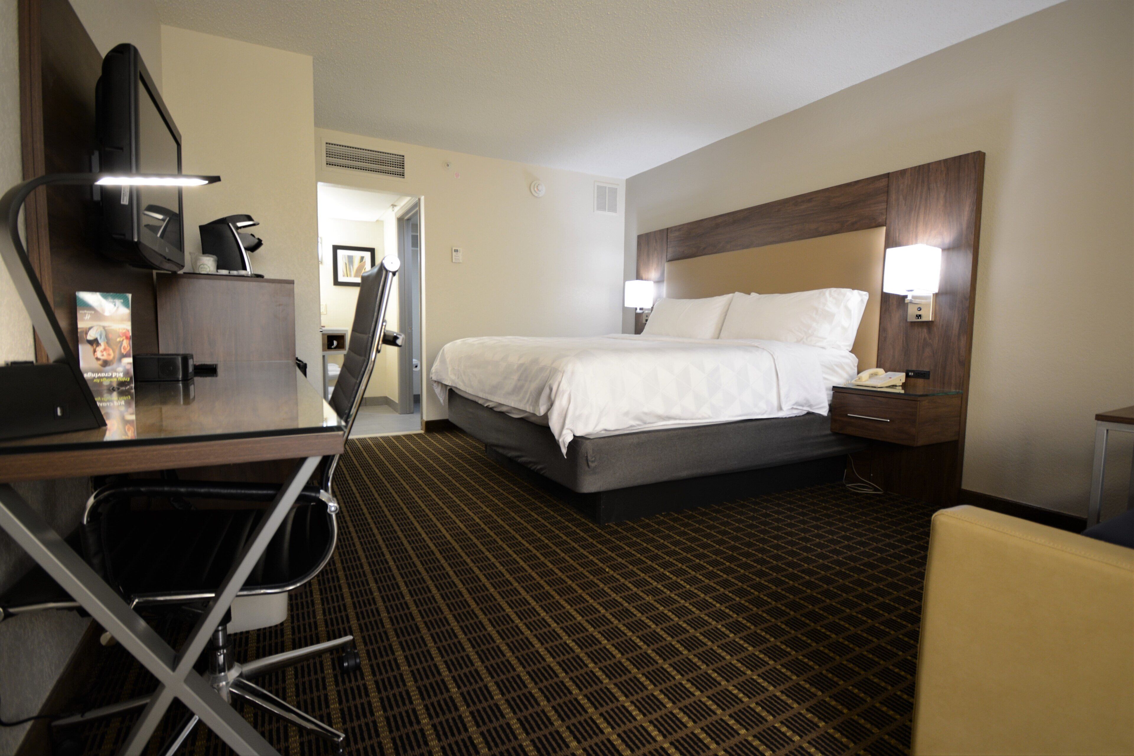 A hotel room with a bed, desk, chair, and a television.