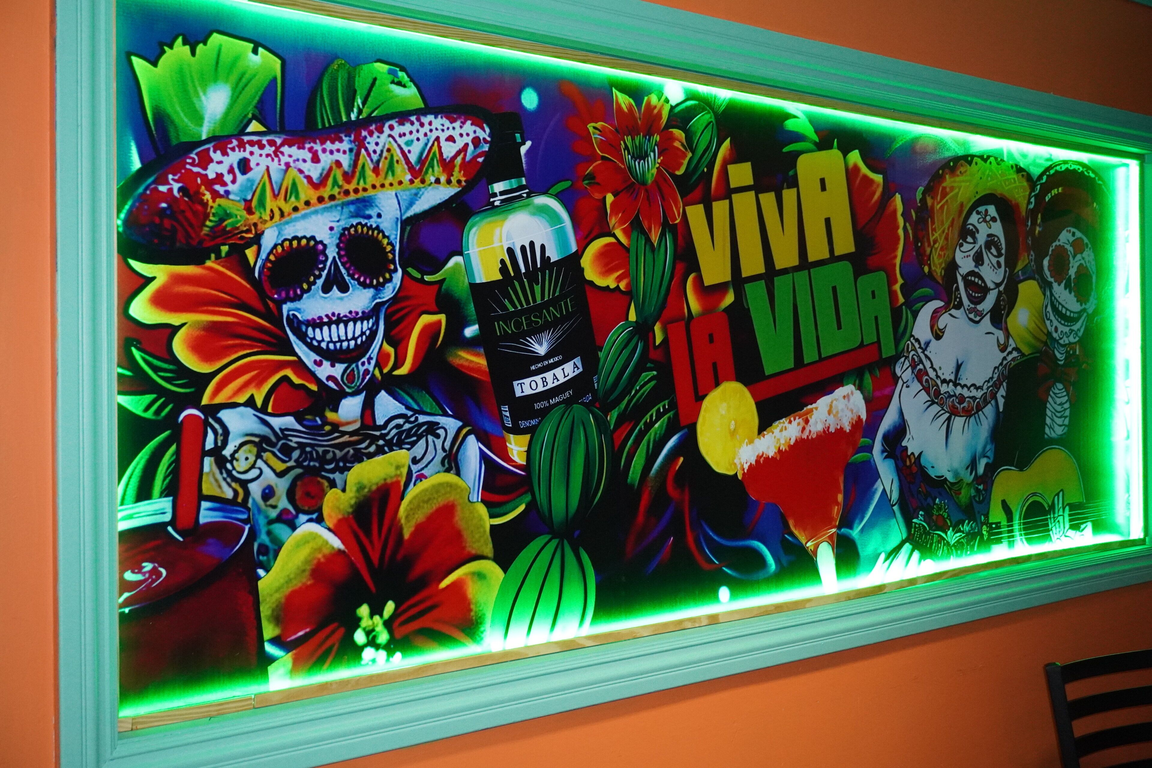 Une fresque colorée ornée de motifs floraux et de têtes de mort éclatants, d’un microphone et de l’inscription « Viva Vida ».