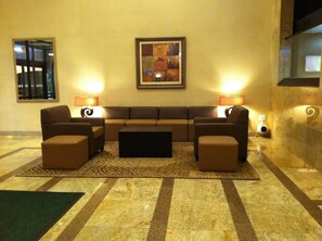 A hotel lobby with a sofa set, two lamps, a framed artwork, and a patterned rug. - Holiday Inn Hazlet by IHG (Hazlet)