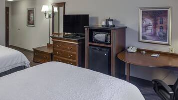 A hotel room with two beds, a desk with a telephone, a microwave, a coffee maker, and a television.